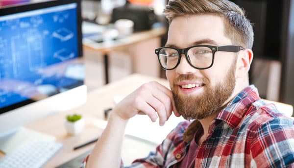 Mann mit Brille und Vollbart vor dem Monitor, der sich zum Betrachter umdreht.