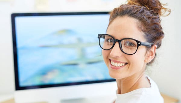 Junge Frau vor dem Monitor, die sich zum Betrachter umdreht.