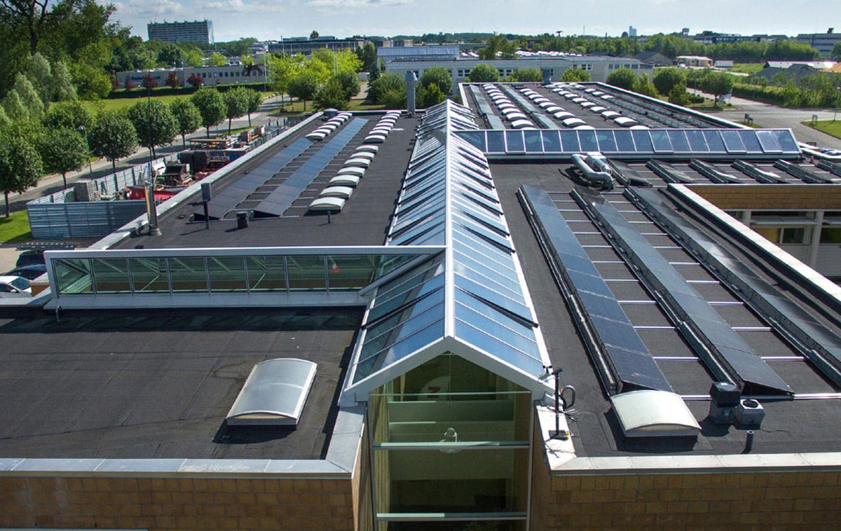 Gebäudeverbindende Satteldach-Lichtbänder Gebäudeverbindende Satteldach-Lichtbänder mit weißem Rahmen. Foto des Gebäudekomplexes aus der Vogelperspektive.